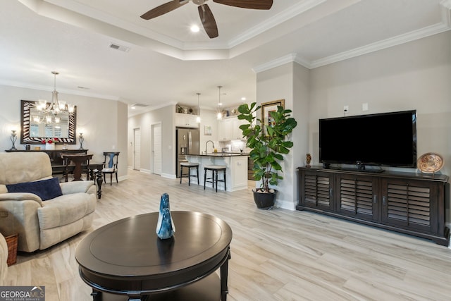 living room featuring crown molding, sink, light hardwood / wood-style floors, and a tray ceiling