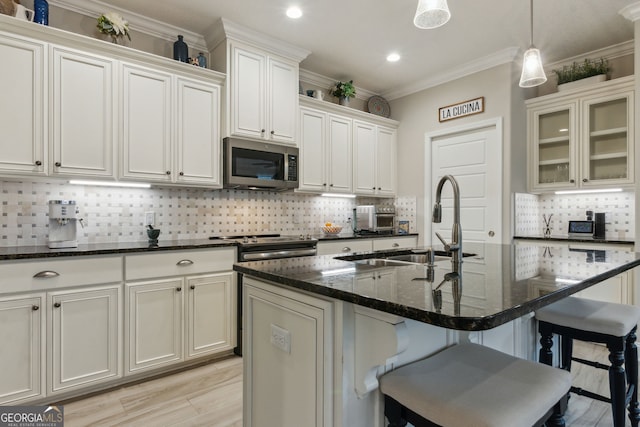 kitchen with pendant lighting, appliances with stainless steel finishes, a center island with sink, and dark stone countertops