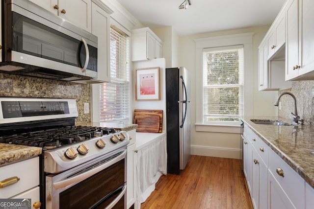 kitchen with sink, stainless steel appliances, tasteful backsplash, light stone countertops, and white cabinets