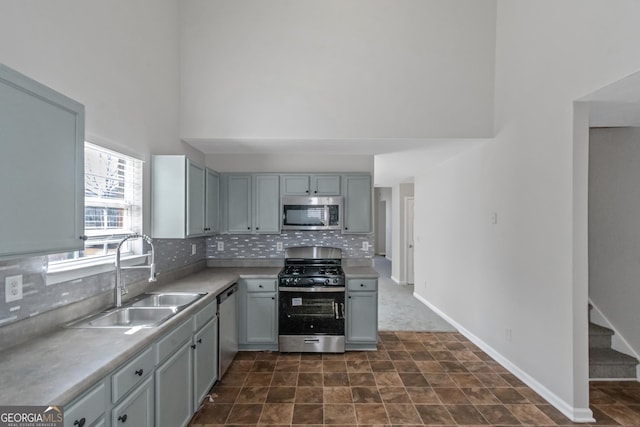 kitchen with sink, gray cabinets, appliances with stainless steel finishes, backsplash, and a high ceiling