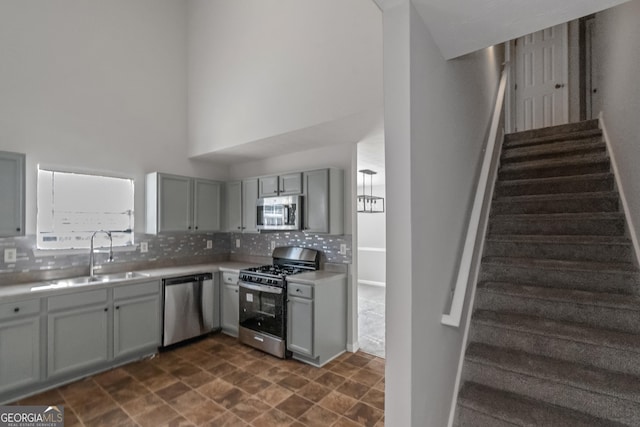 kitchen with sink, gray cabinetry, a towering ceiling, stainless steel appliances, and tasteful backsplash