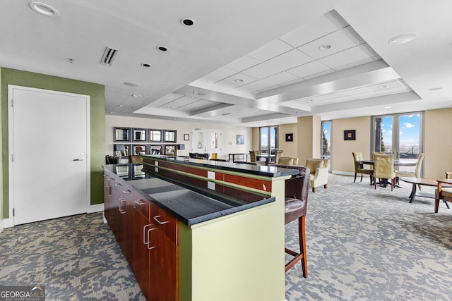 kitchen featuring visible vents, a breakfast bar, a kitchen island, dark countertops, and dark carpet