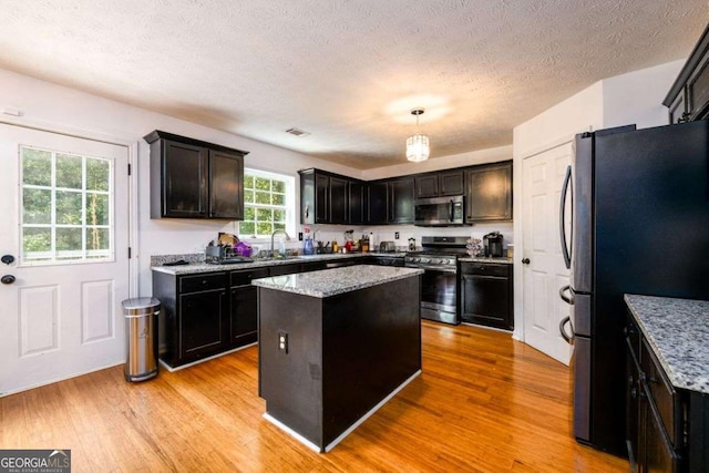 kitchen featuring light wood-type flooring, light stone countertops, a kitchen island, and appliances with stainless steel finishes