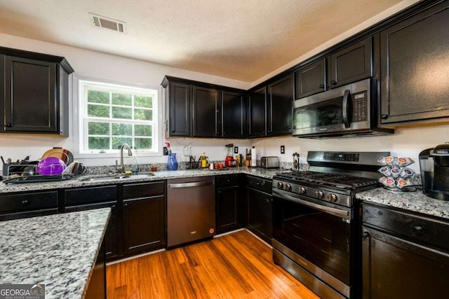 kitchen featuring visible vents, dark wood-style floors, appliances with stainless steel finishes, light stone countertops, and a sink