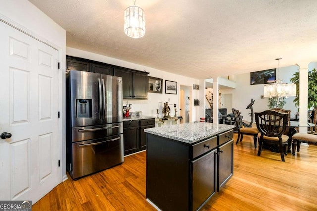 kitchen featuring light stone counters, stainless steel refrigerator with ice dispenser, a center island, light wood finished floors, and pendant lighting