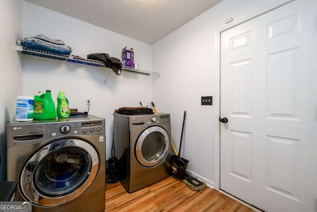 laundry area featuring washer and clothes dryer, light wood-style floors, a textured ceiling, laundry area, and baseboards