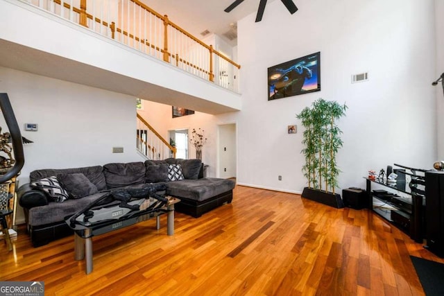 living room featuring visible vents, a ceiling fan, a towering ceiling, stairway, and wood finished floors