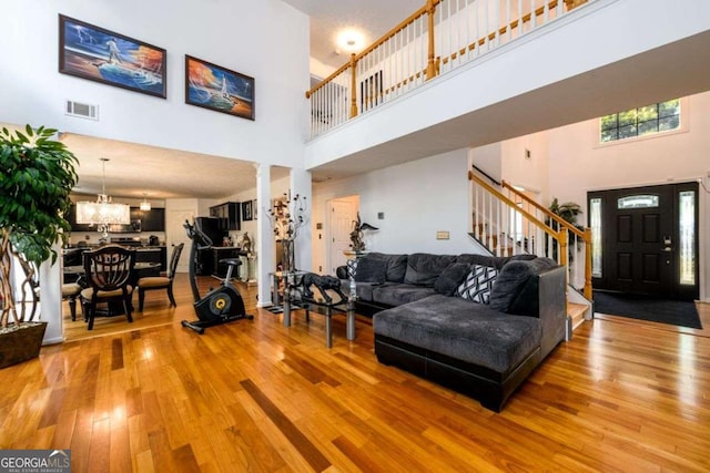 living room with a notable chandelier, a high ceiling, visible vents, light wood-style floors, and stairs