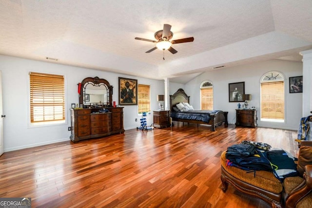 bedroom with a textured ceiling, decorative columns, multiple windows, and wood finished floors