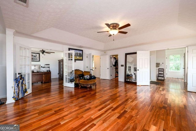 unfurnished living room featuring a textured ceiling, a tray ceiling, french doors, and wood finished floors