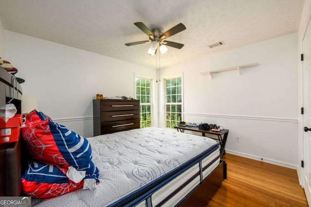 bedroom with visible vents, a ceiling fan, a textured ceiling, wood finished floors, and baseboards