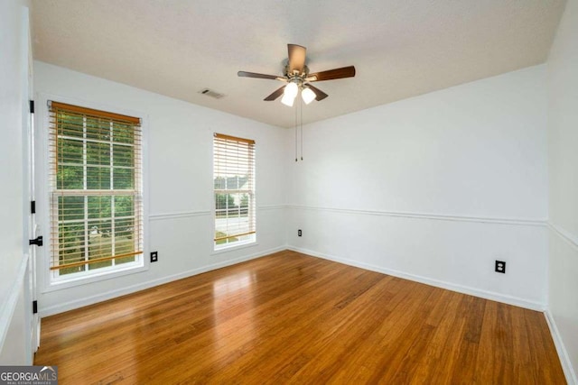 empty room with visible vents, ceiling fan, baseboards, and wood finished floors