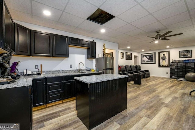 kitchen with dark cabinets, a kitchen island, a sink, freestanding refrigerator, and light wood finished floors