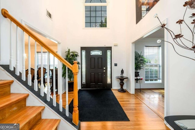 foyer with stairway, a high ceiling, visible vents, and wood finished floors