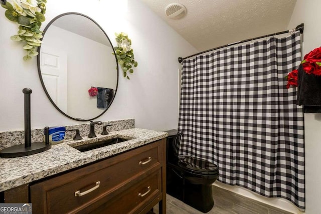 full bathroom with visible vents, toilet, vanity, a textured ceiling, and wood finished floors