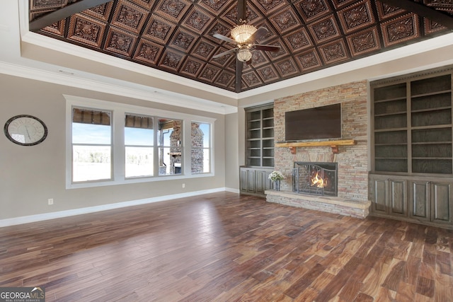 unfurnished living room featuring built in shelves, a stone fireplace, crown molding, a tray ceiling, and hardwood / wood-style flooring