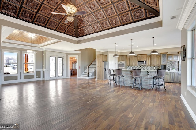 kitchen with a raised ceiling, a breakfast bar area, decorative backsplash, hanging light fixtures, and stainless steel appliances