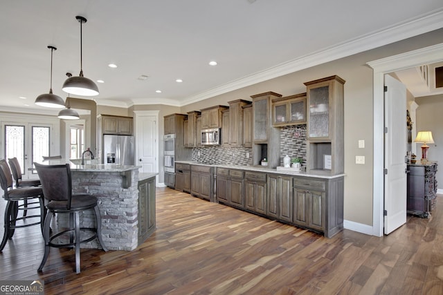 kitchen featuring dark hardwood / wood-style floors, pendant lighting, tasteful backsplash, stainless steel appliances, and a center island with sink