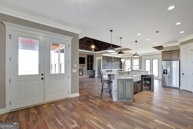 kitchen with sink, stainless steel fridge with ice dispenser, hanging light fixtures, a kitchen breakfast bar, and an island with sink