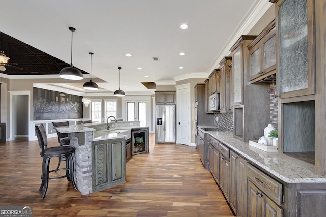 kitchen with a large island, hanging light fixtures, appliances with stainless steel finishes, beverage cooler, and light stone countertops