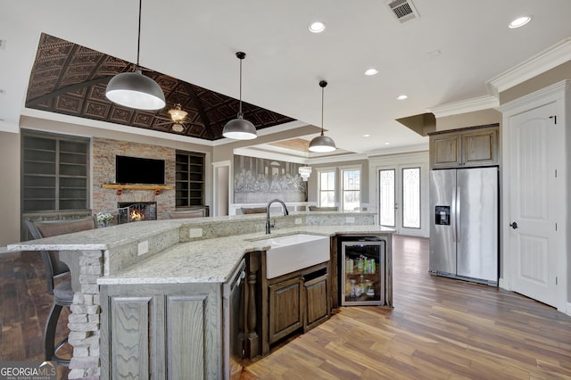 kitchen featuring sink, crown molding, stainless steel fridge, wine cooler, and light stone countertops