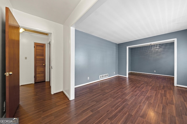 empty room featuring dark wood-type flooring, visible vents, and baseboards