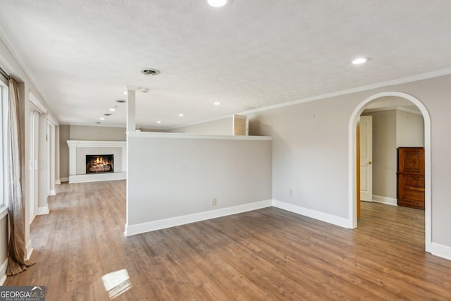 213 Pine Crest Dr, Cumming, GA 30040 - unfurnished living room with wood finished floors, recessed lighting, a warm lit fireplace, crown molding, and arched walkways