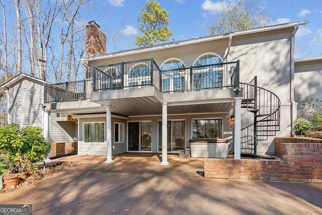 back of property with a hot tub, a patio, and a balcony