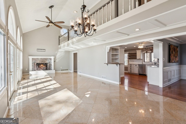 unfurnished living room featuring a premium fireplace, ceiling fan with notable chandelier, and high vaulted ceiling