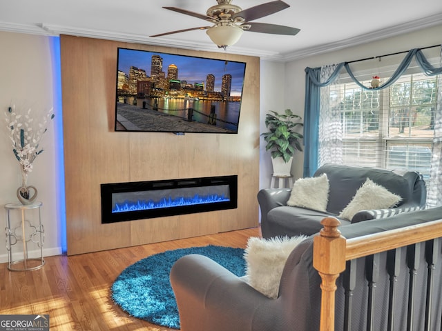 living area featuring crown molding, a glass covered fireplace, ceiling fan, wood finished floors, and baseboards