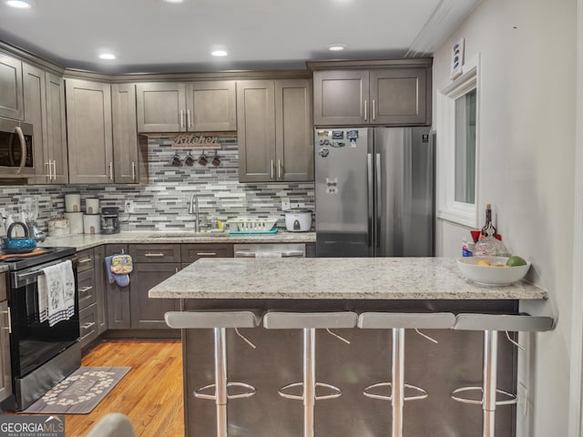 kitchen featuring tasteful backsplash, stainless steel appliances, a sink, and light wood-style flooring