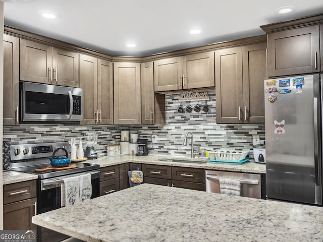 kitchen with tasteful backsplash, light stone counters, stainless steel appliances, a sink, and recessed lighting