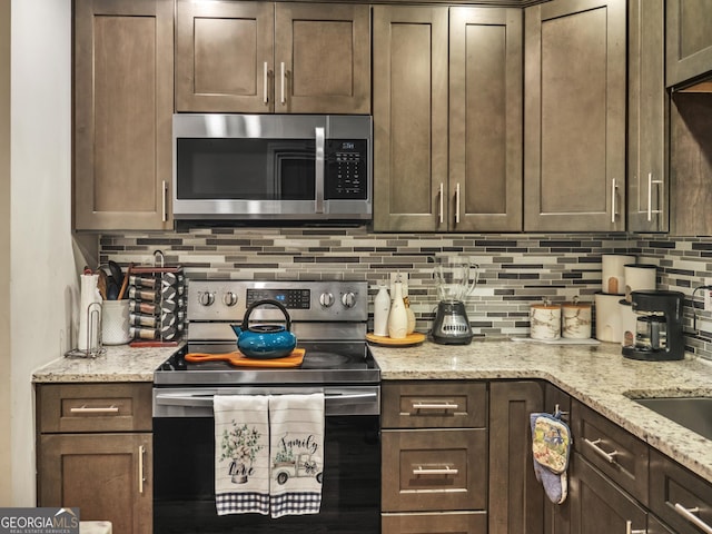 kitchen featuring dark brown cabinets, backsplash, light stone countertops, electric range oven, and stainless steel microwave