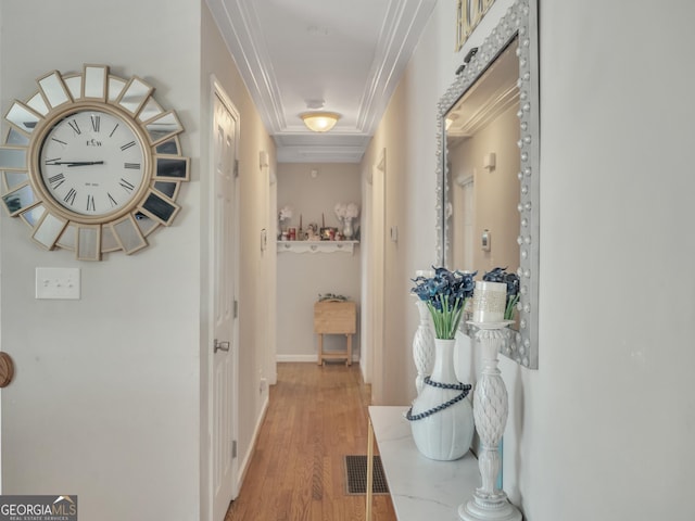 hallway with light wood-style flooring, visible vents, baseboards, and ornamental molding