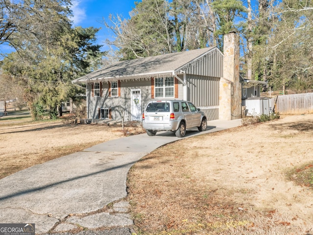 view of front of home featuring driveway, a chimney, and fence