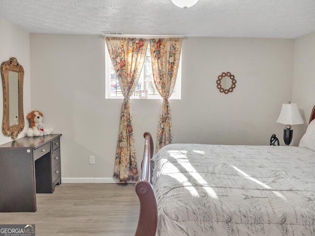 bedroom featuring a textured ceiling, light wood finished floors, visible vents, and baseboards