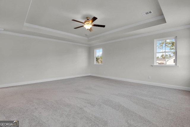 carpeted spare room featuring visible vents, a tray ceiling, crown molding, baseboards, and ceiling fan