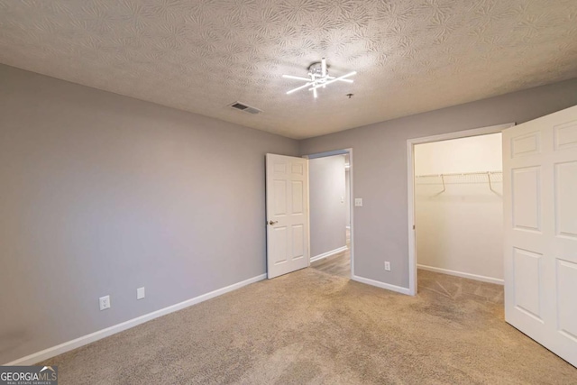 unfurnished bedroom featuring ceiling fan, a textured ceiling, a walk in closet, light colored carpet, and a closet