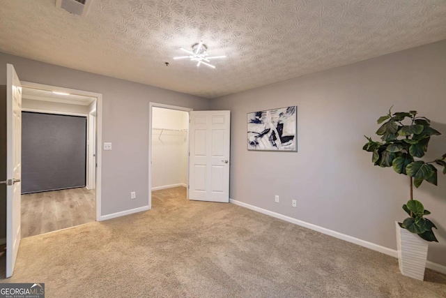 unfurnished bedroom featuring light colored carpet, a closet, a textured ceiling, and a walk in closet