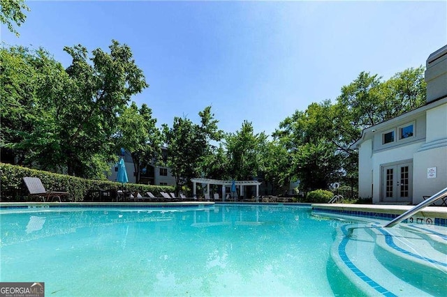 view of pool with french doors and a pergola