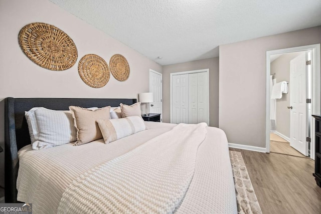 bedroom with a closet, ensuite bath, light hardwood / wood-style floors, and a textured ceiling