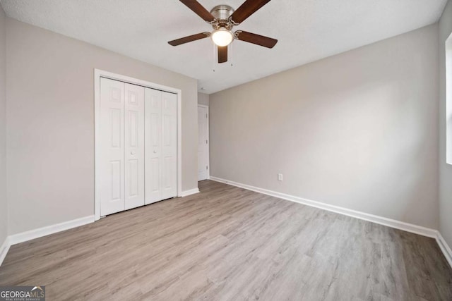 unfurnished bedroom with ceiling fan, a textured ceiling, a closet, and light wood-type flooring