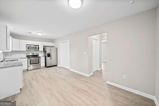 kitchen featuring appliances with stainless steel finishes, sink, white cabinets, light stone counters, and light hardwood / wood-style flooring