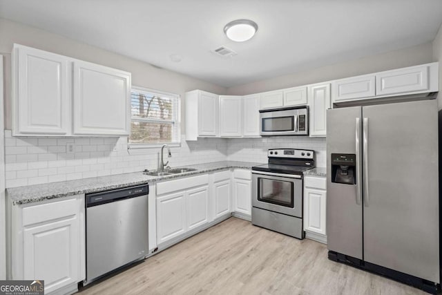 kitchen with appliances with stainless steel finishes, sink, white cabinets, light hardwood / wood-style floors, and light stone countertops