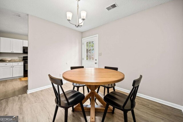 dining area with a chandelier, a textured ceiling, and light wood-type flooring