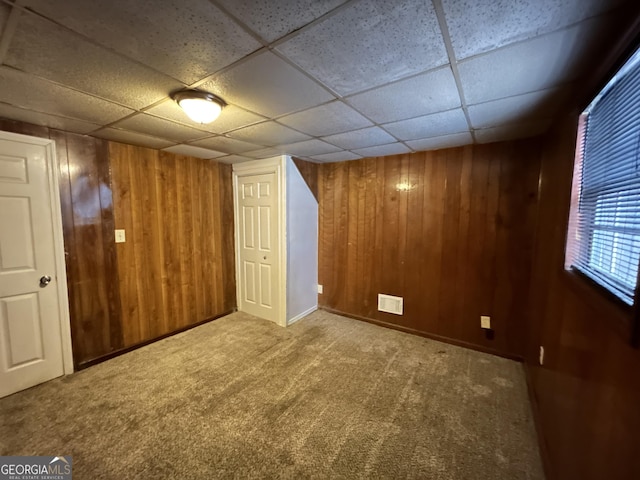 basement featuring carpet flooring, a paneled ceiling, and wood walls