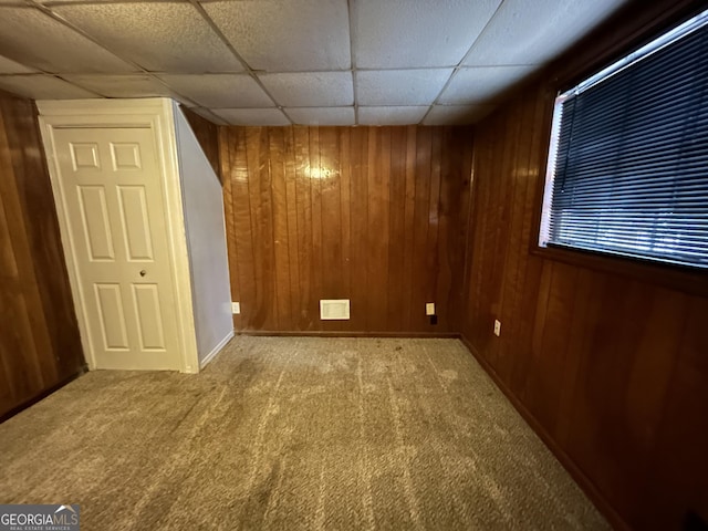 interior space with wooden walls, carpet flooring, and a drop ceiling