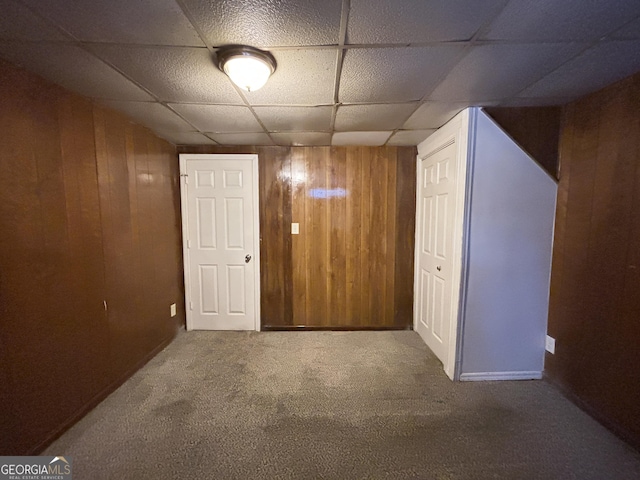 interior space with carpet floors, a paneled ceiling, and wood walls