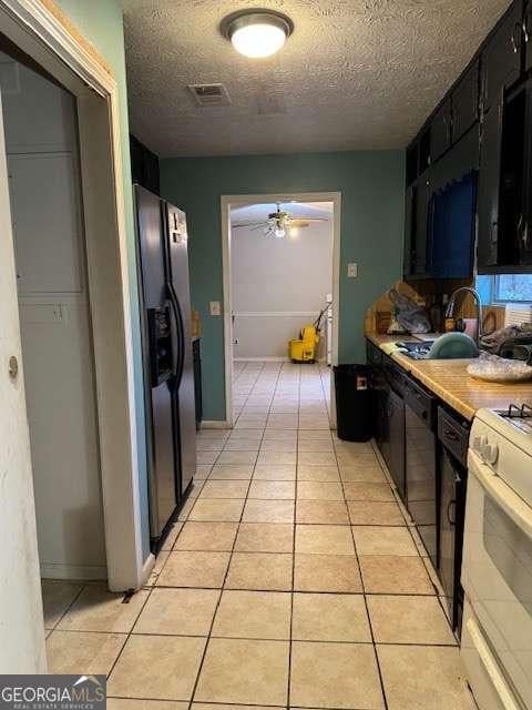 kitchen with sink, gas range gas stove, stainless steel fridge with ice dispenser, a textured ceiling, and light tile patterned floors