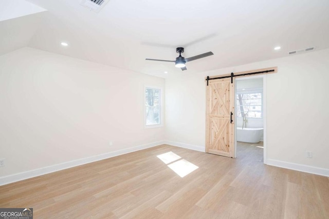 unfurnished bedroom with ceiling fan, a barn door, and light hardwood / wood-style floors